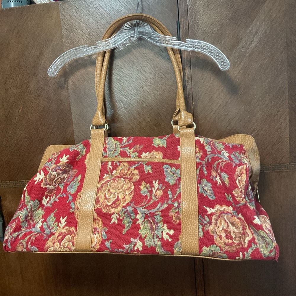 Red floral tapestry travel duffel bag features brown leather handles and accents